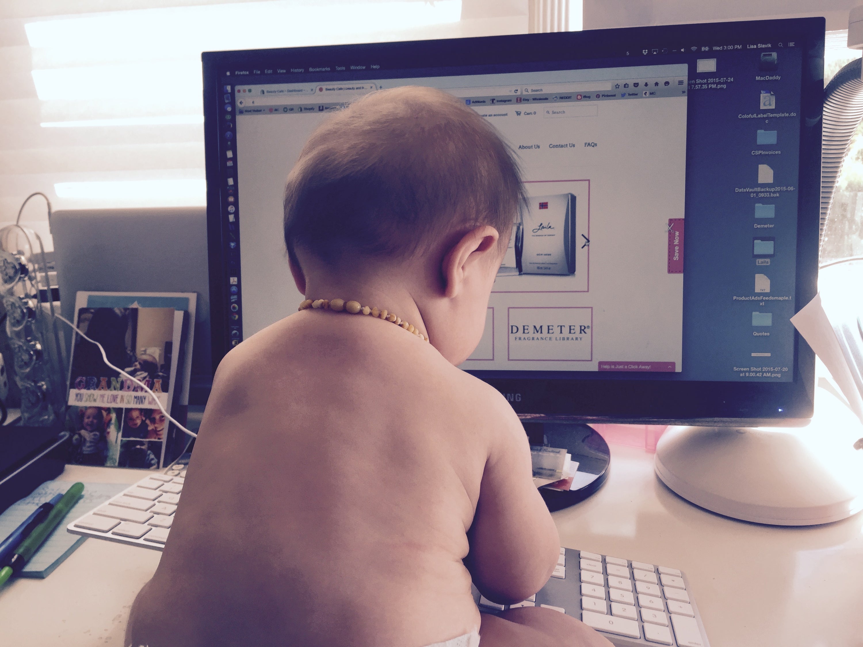 Baby sitting in front of a computer screen on a desk