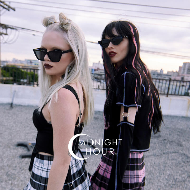 Two women wearing sunglasses and plaid outfits on a rooftop with 'Midnight Hour' branding.