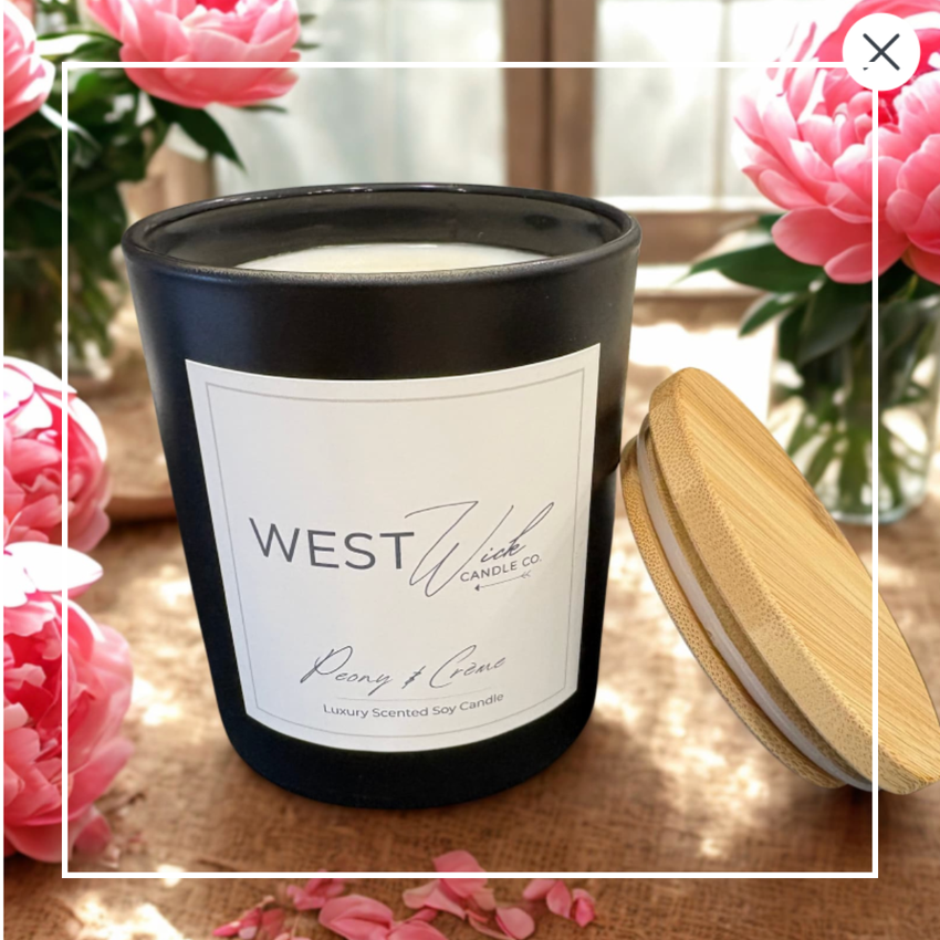 West Wick candle with a wooden lid on a wooden surface with pink flowers in the background